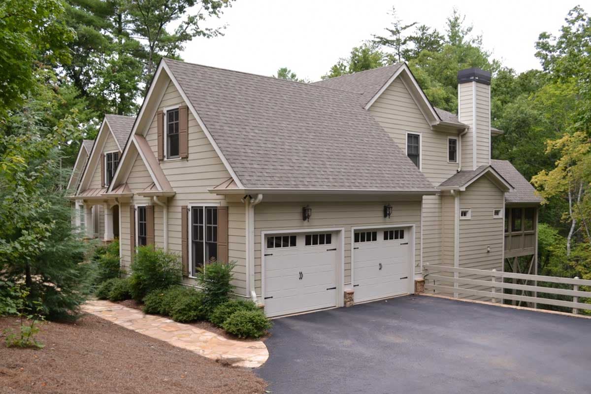 House plan exterior of a multi-story home with a side-entry two-car garage, gables, dormers, and a prominent stone chimney.