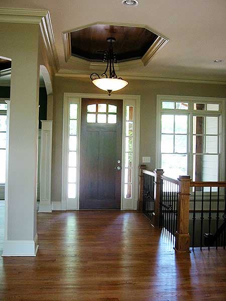 Interior view of house entryway with dark wood door, sidelights, transom windows, and coffered ceiling detail.