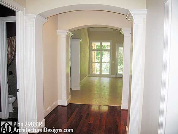 Interior view of a house plan, showing an arched doorway with fluted columns leading to a large room with french doors and windows.