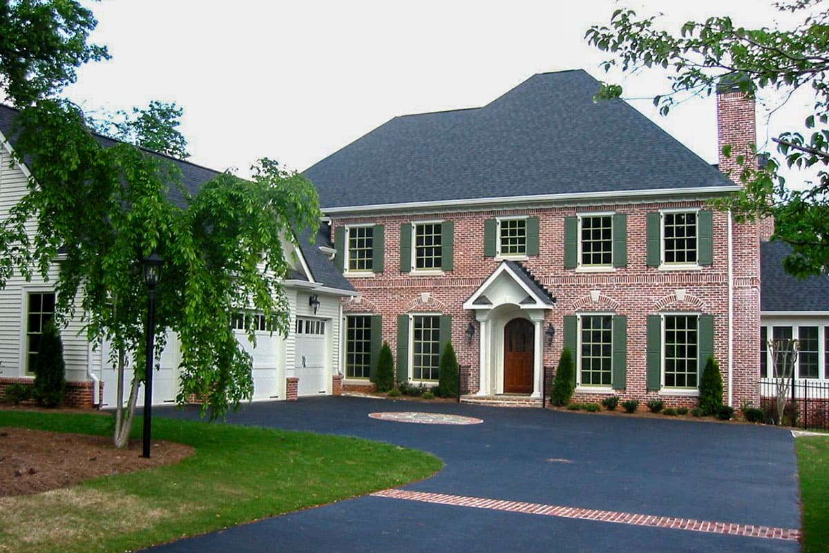 House plan exterior. Two-story brick home with a front gable, multiple windows with green shutters, and a covered entry. Includes an attached garage.