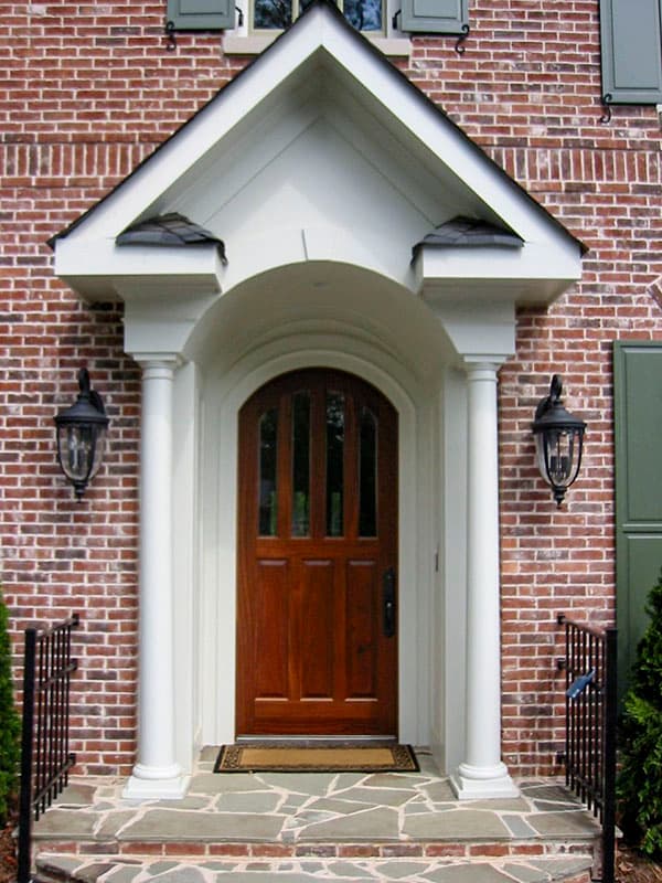 House plan exterior: Brick facade with arched entryway, wood door, gable roof porch, and Doric columns.