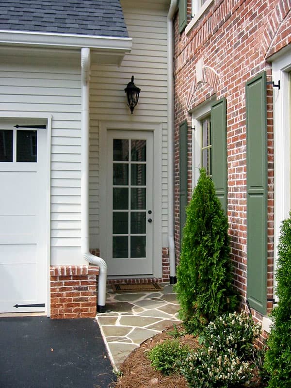 House plan exterior showing garage, paneled door, brick facade, and green shutters.