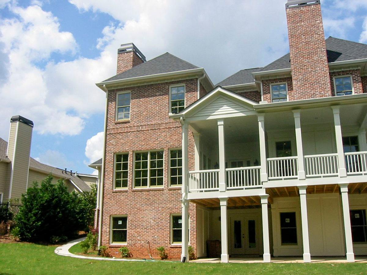 House plan exterior: Brick structure with multiple stories, a covered porch, large windows, and a prominent chimney.