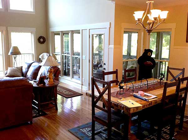Interior view of a great room with vaulted ceiling, large windows, leather sofa, and dining area with wooden table and chairs.