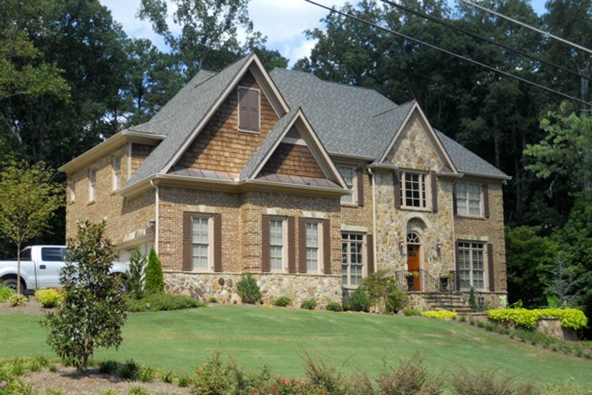 House plan exterior: Two-story home with brick and stone facade, multiple gables, dormers, and a front-facing garage.