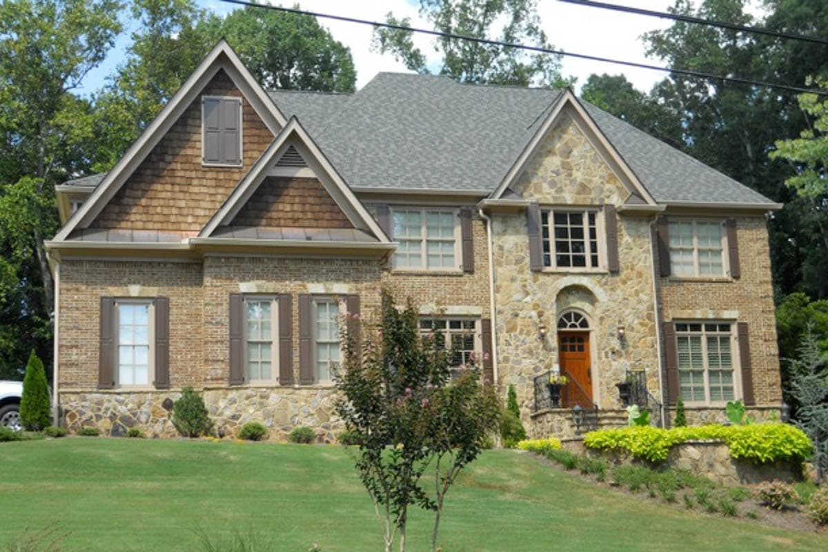 House plan exterior. Two-story with stone and brick facade. Features include gables, multiple dormers, and a prominent front entry.