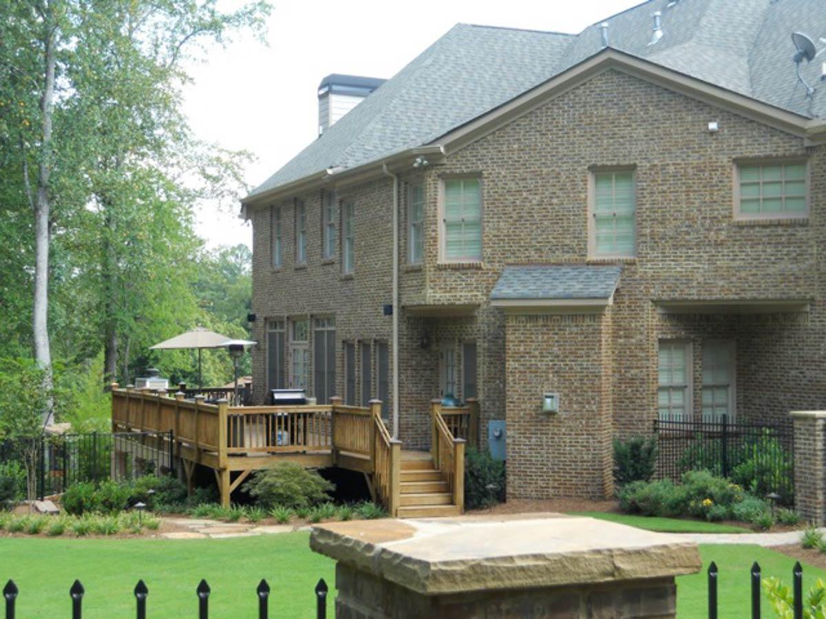 Two-story brick house plan exterior with a large wooden deck, multiple gables, and visible window grids.