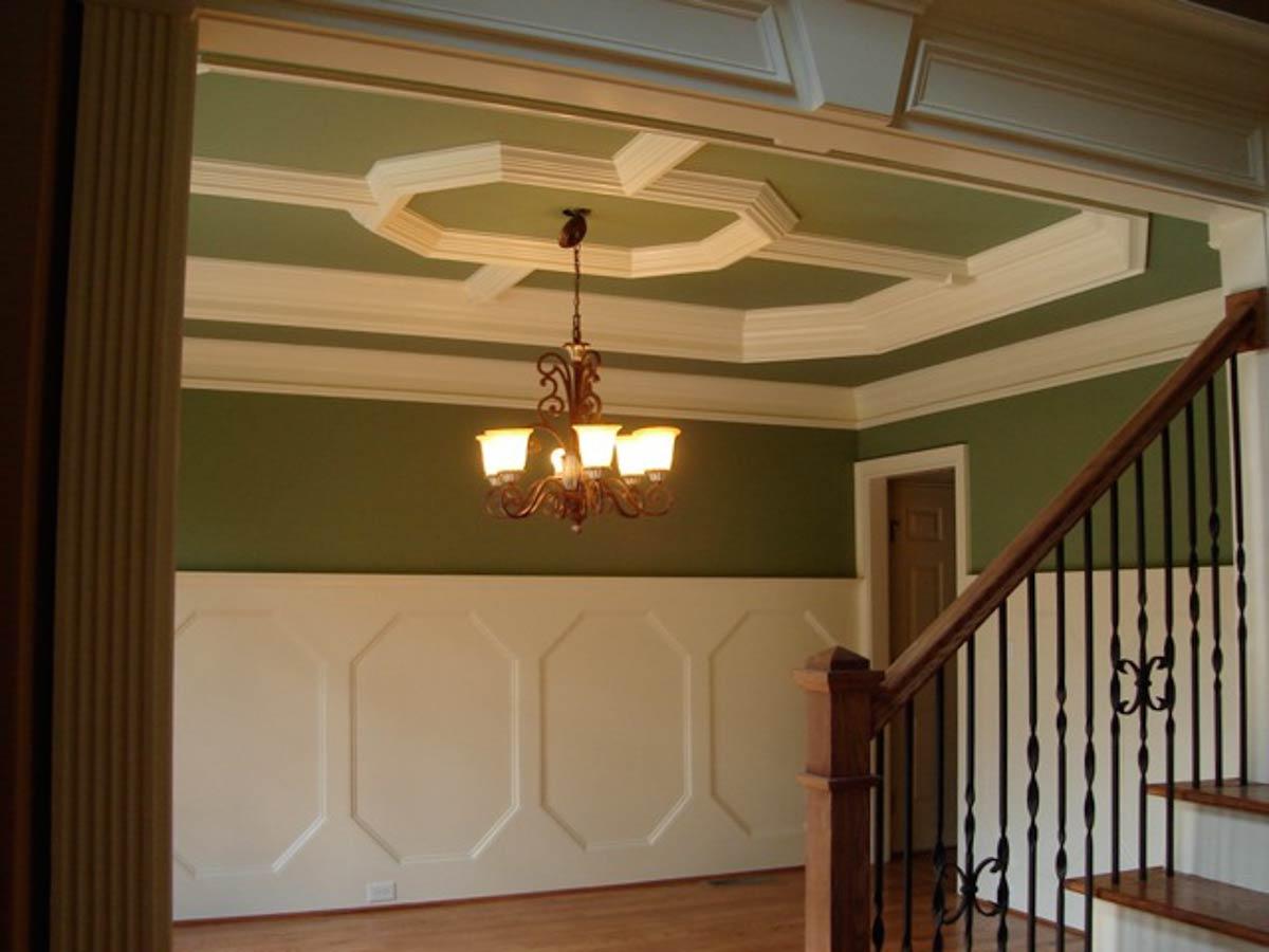 Interior view of a dining room with coffered ceiling, wainscoting, chandelier, and staircase with wrought iron railings.