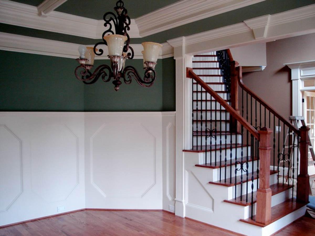 Interior view showing a grand staircase with wooden treads, black balusters, and paneled wainscoting.