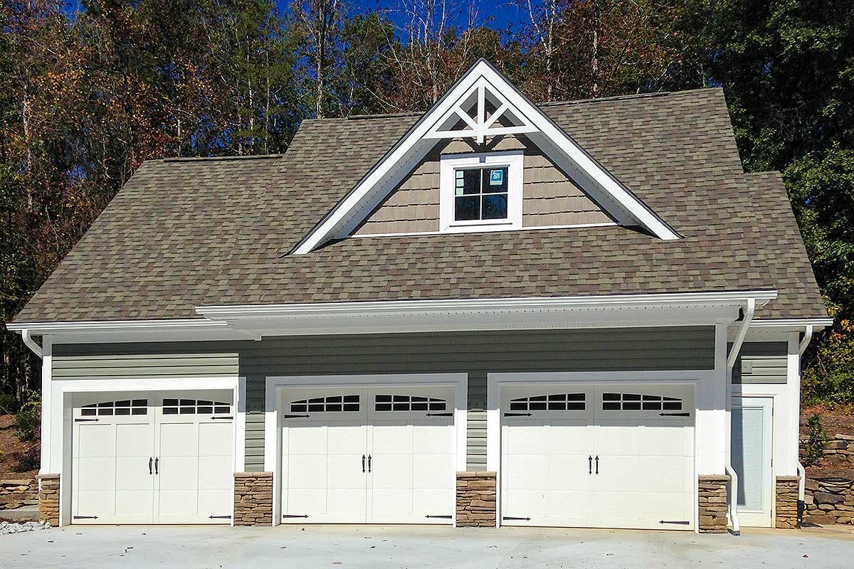 House plan exterior. Two-story garage with three-bay garage door, gabled dormer with decorative trim, and stone accents.