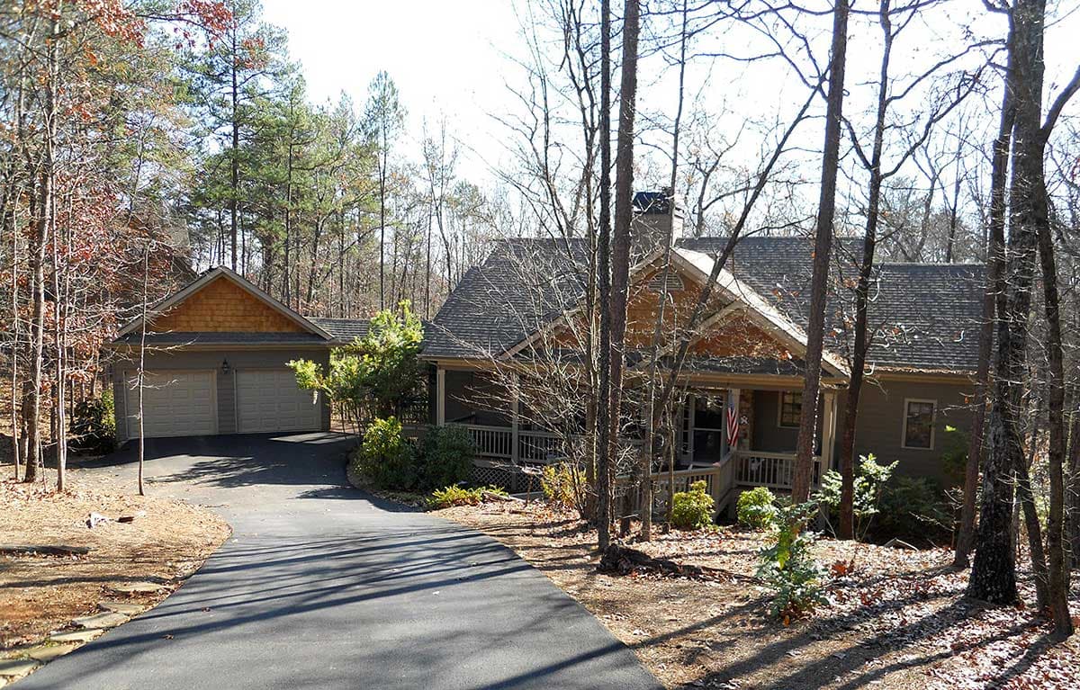 House plan exterior: one-story dwelling with wraparound porch, gabled dormer, and attached two-car garage.