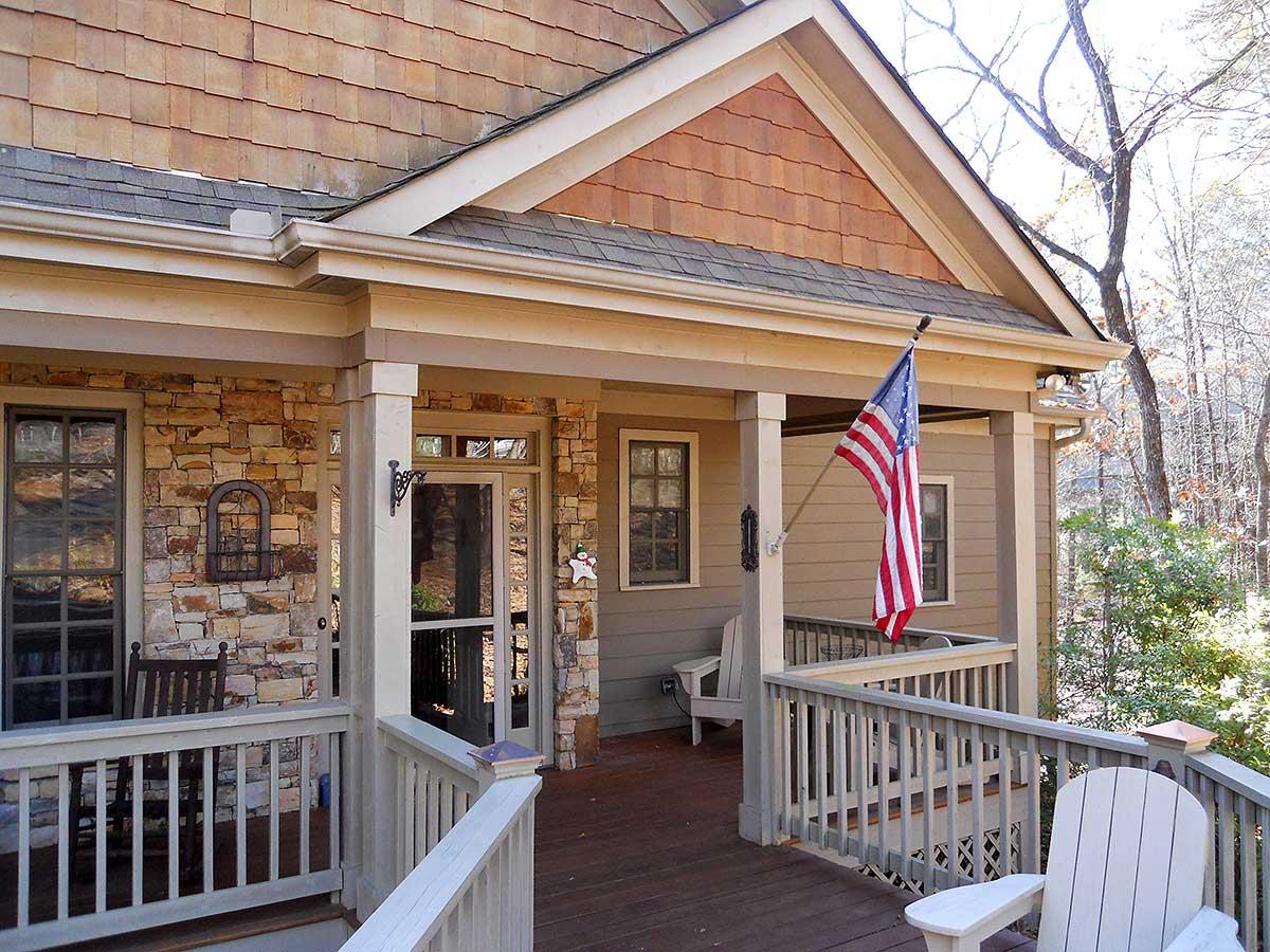 House plan exterior features stone foundation, wood siding, covered porch with columns, gabled dormer, and multiple windows.