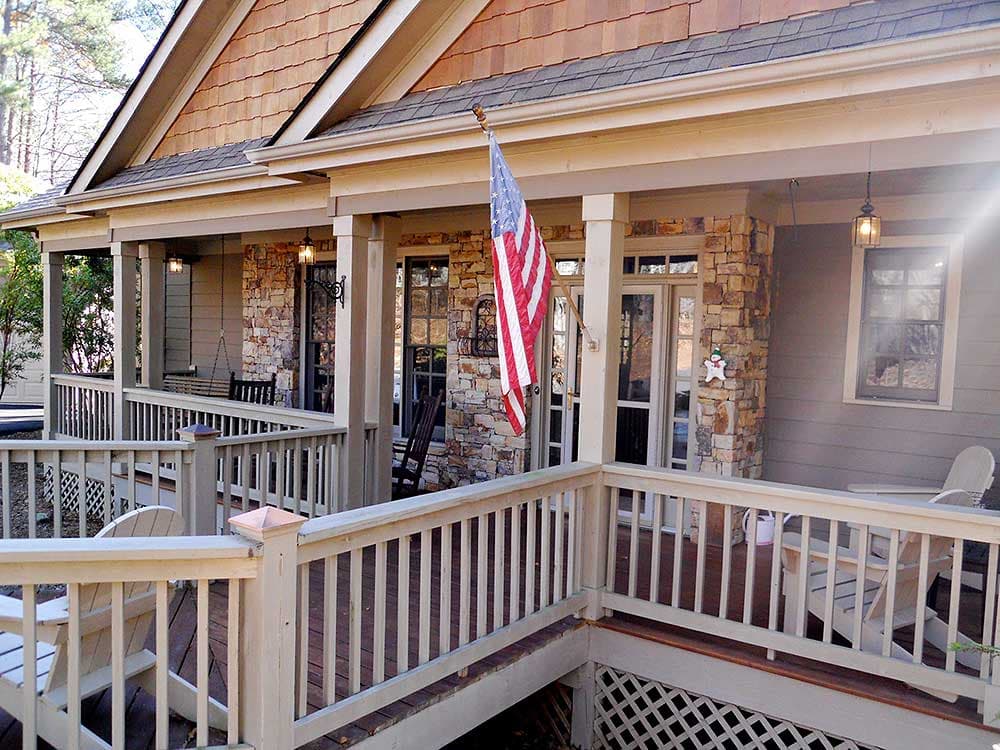 House plan exterior features a wide wraparound porch with stone accents, gabled rooflines, and wood siding.
