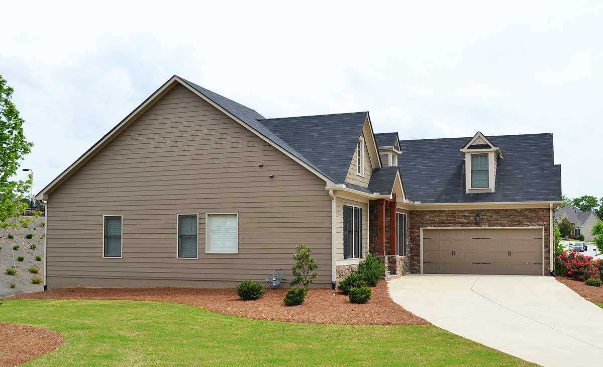 House plan exterior: Side view of a two-story house with vinyl siding, gables, dormers, and a two-car garage.
