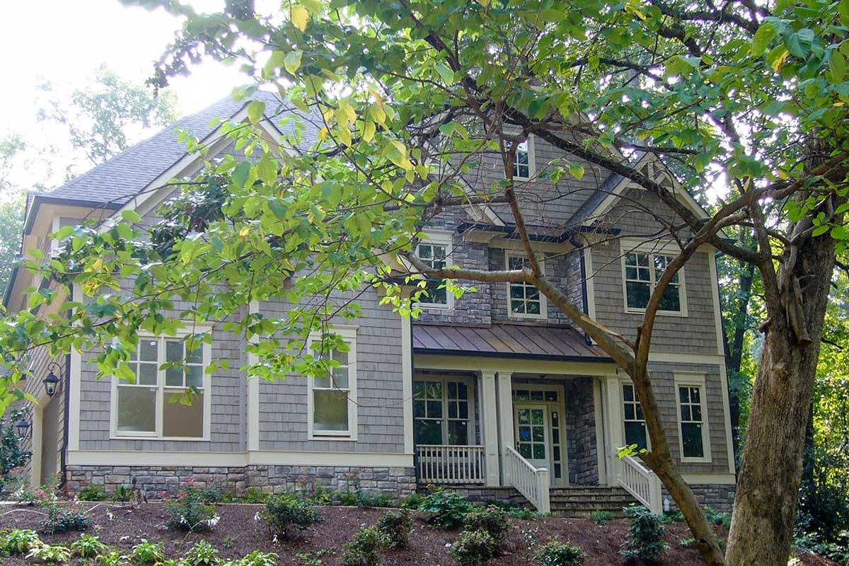 House plan exterior: Two-story home with stone and shingle siding, gables, and a covered front porch with metal roof.