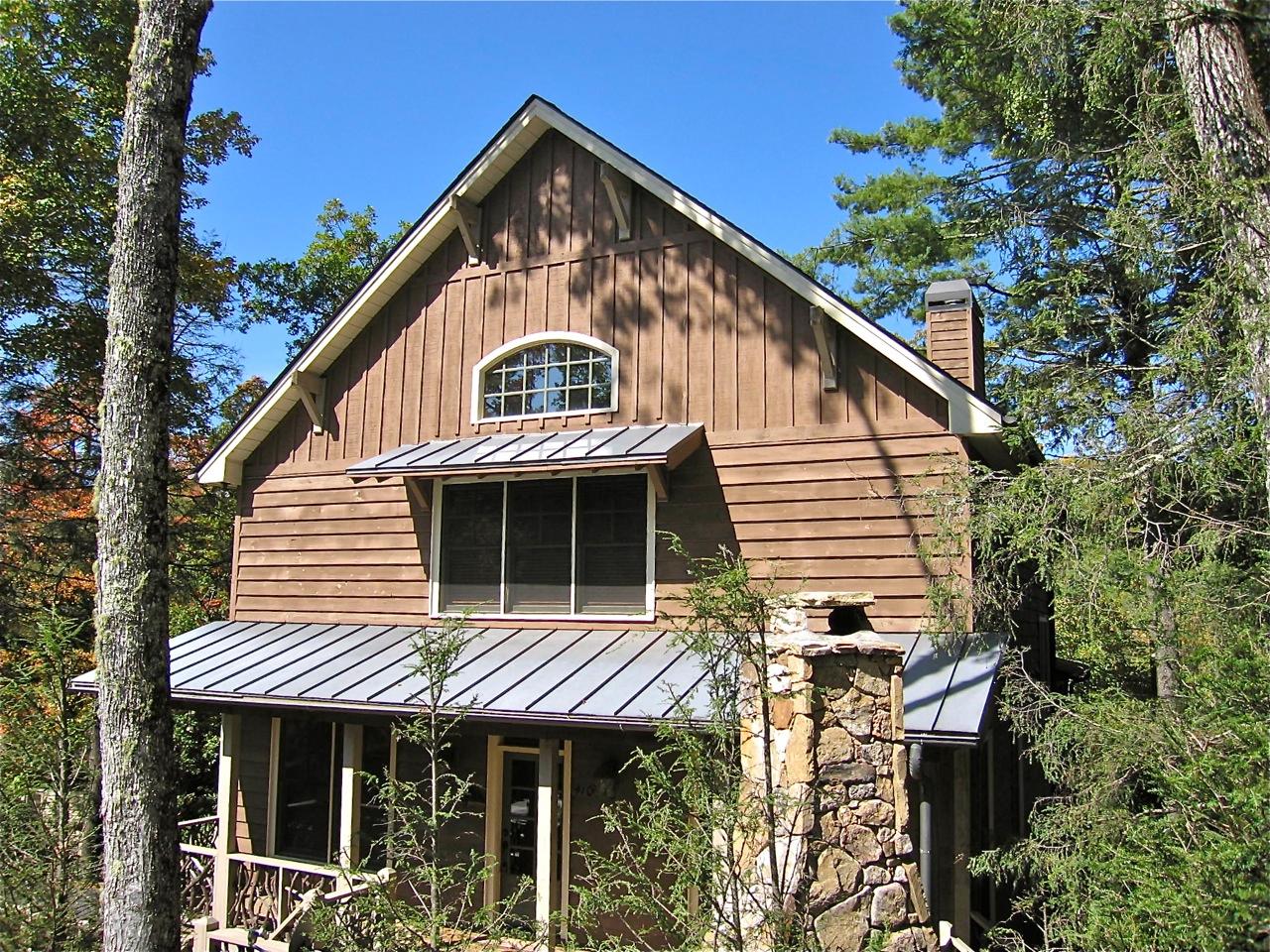 House plan exterior, two stories, wood siding, metal roof, stone chimney, and front porch with natural wood railing.