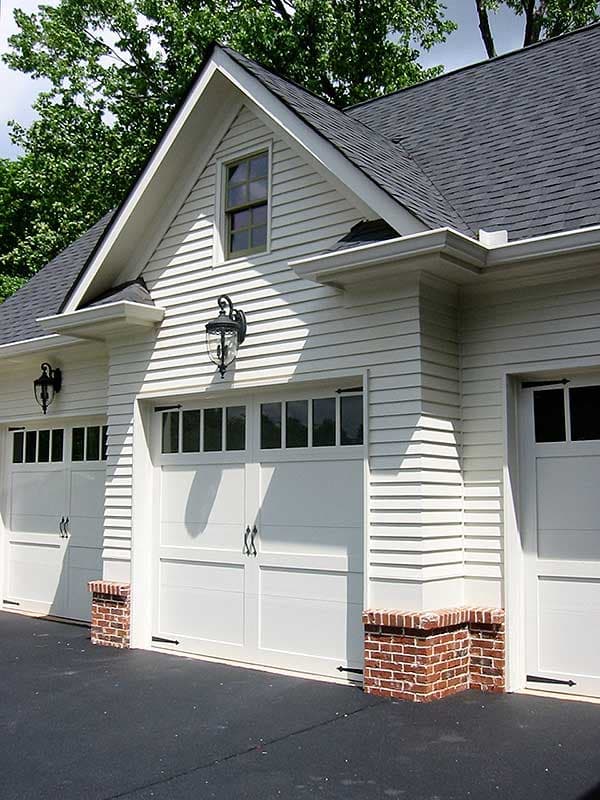 House plan exterior featuring a three-car garage with white paneled doors, brick bases, and a prominent gable dormer.