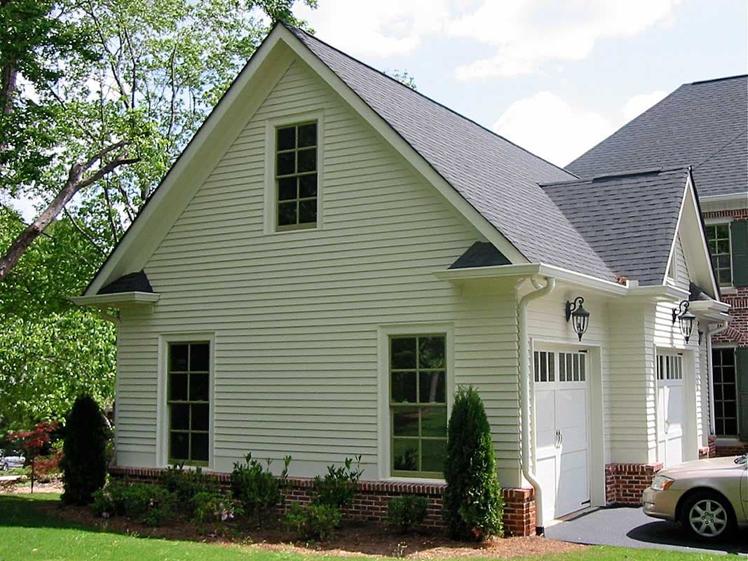 House plan exterior with vinyl siding, gable dormer, two-car garage, and brick foundation.