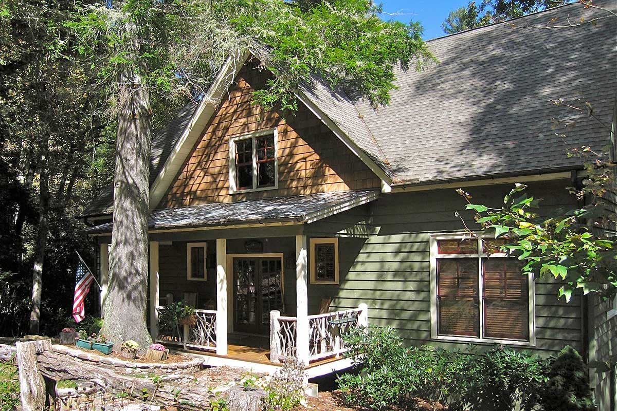 House plan exterior: Two-story home with a prominent front gable, shingle siding and covered porch with decorative railings.