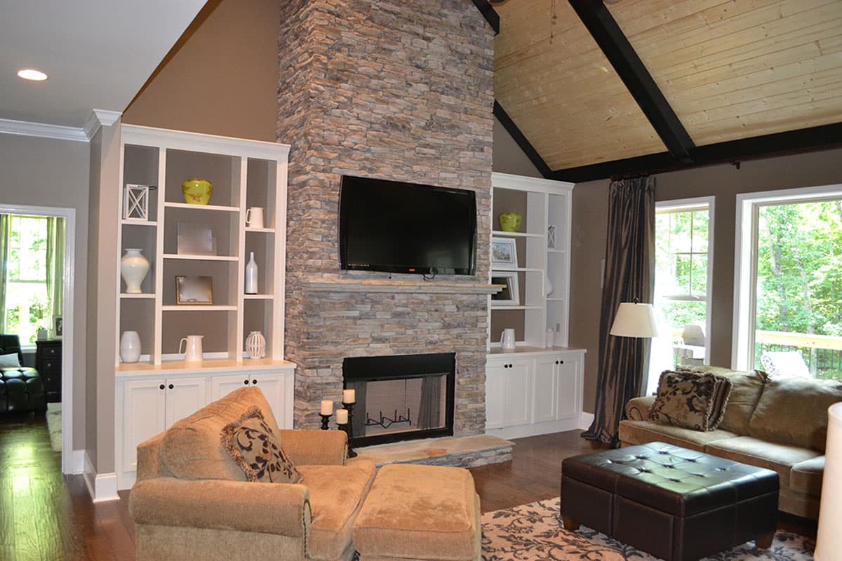 Living room with stone fireplace, built-in shelving, and vaulted, wood-paneled ceiling.