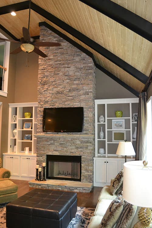 Great room with vaulted, wood-paneled ceiling, exposed beams, stone fireplace, and built-in shelving.
