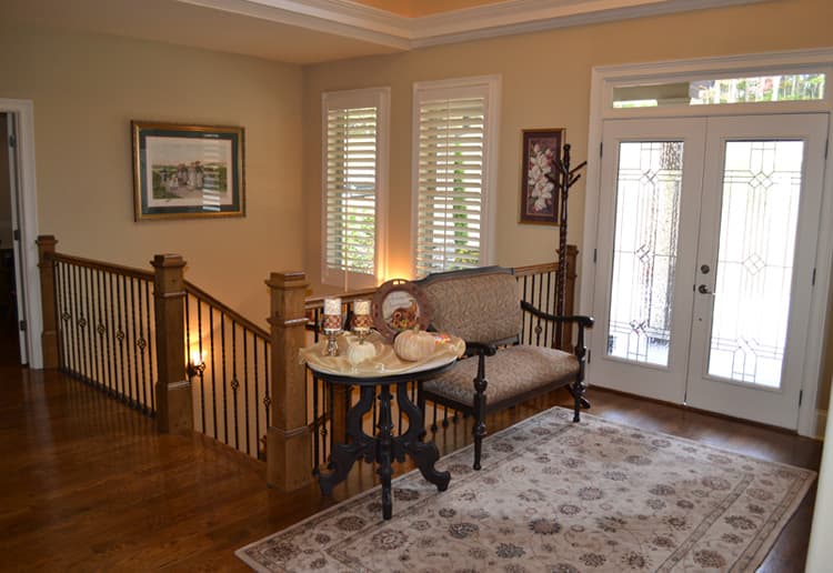 Foyer with double doors, staircase with wrought iron spindles, and two windows with plantation shutters.