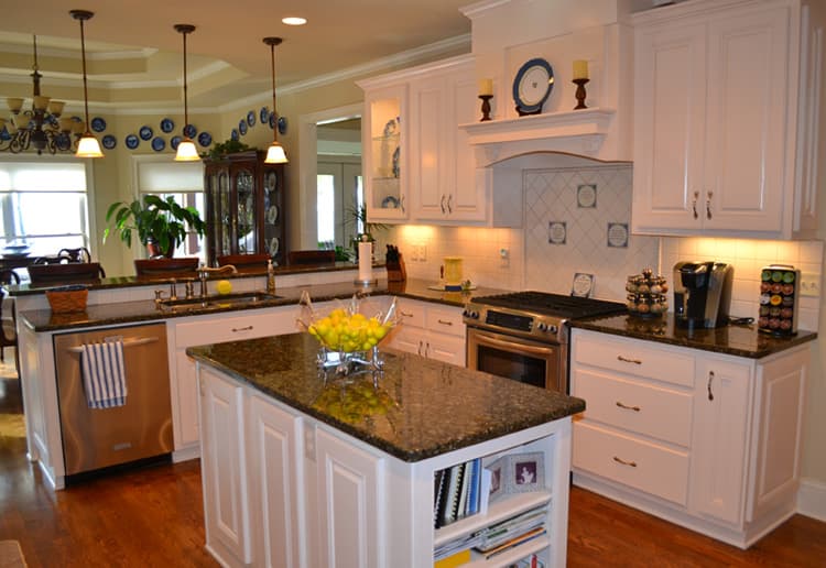 Kitchen interior with island, granite countertops, stainless steel appliances, white cabinetry, and pendant lighting.