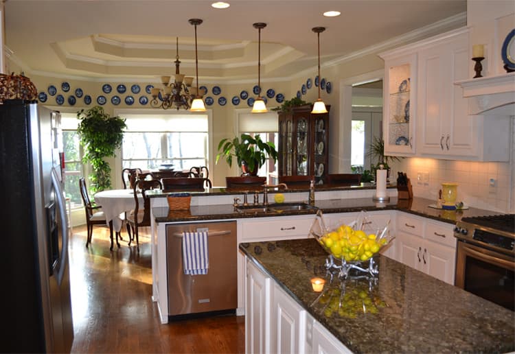 Kitchen with granite countertops, white cabinetry, stainless steel dishwasher, and a dining area with large windows.