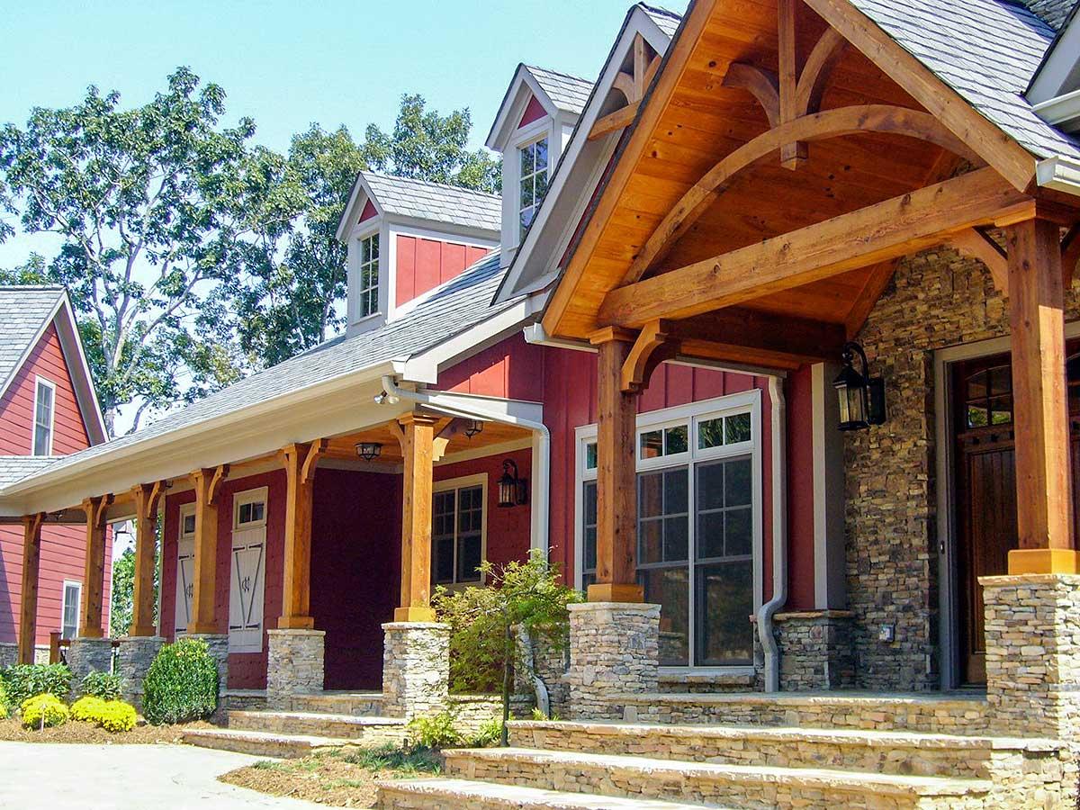 House plan exterior featuring timber framing, stone accents, a covered porch with arched supports, and dormers.