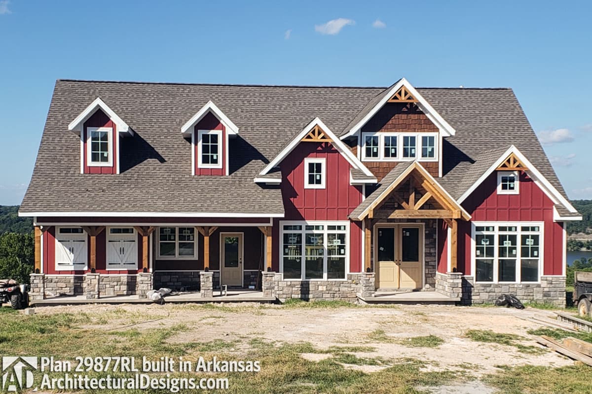 House plan exterior: Two-story Modern Farmhouse with stone accents, prominent gables, exposed rafter tails, and a covered porch with timber supports.
