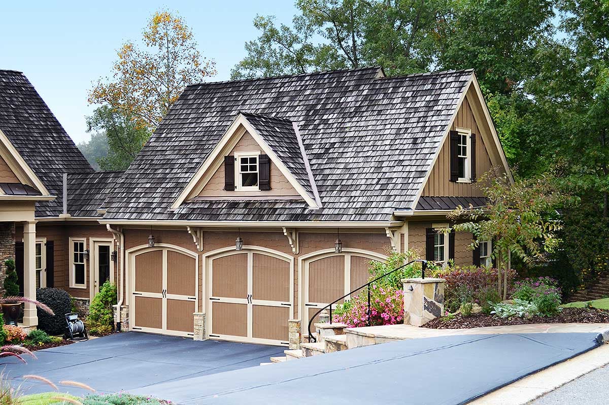 House plan exterior featuring a three-car garage with arched doors, dormers, and a complex roofline.