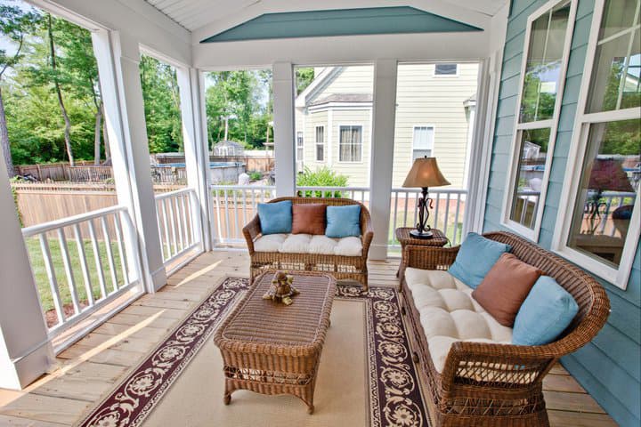 Screened porch with wicker seating, coffee table, rugs, and view of backyard pool and neighboring houses.