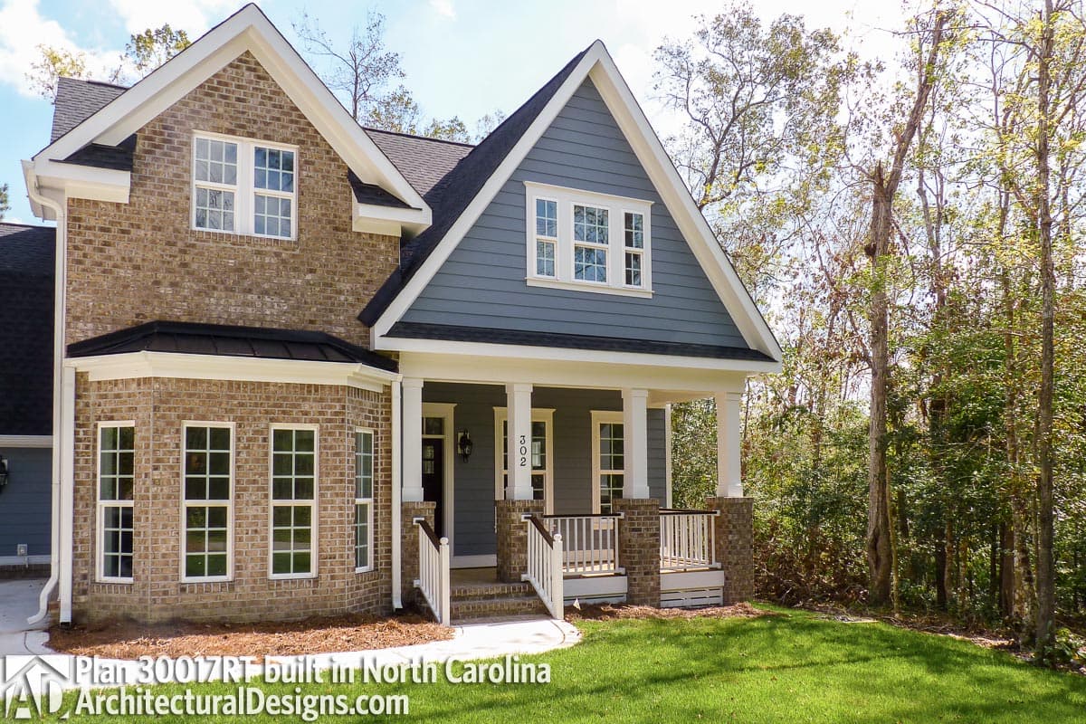 Two-story house plan exterior with brick facade, blue siding, gabled dormer, and covered front porch with white columns.