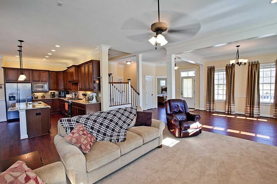 Open concept living area with kitchen island, dark wood cabinets, staircase, and large windows with draped curtains.
