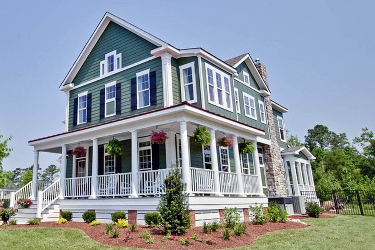 House plan exterior: Two-story green home with wrap-around porch, dormer windows, and stone chimney.