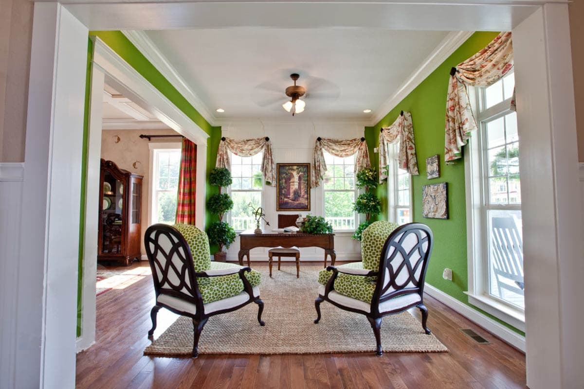 Home office with a desk, two accent chairs, and decorative plants flanking windows.