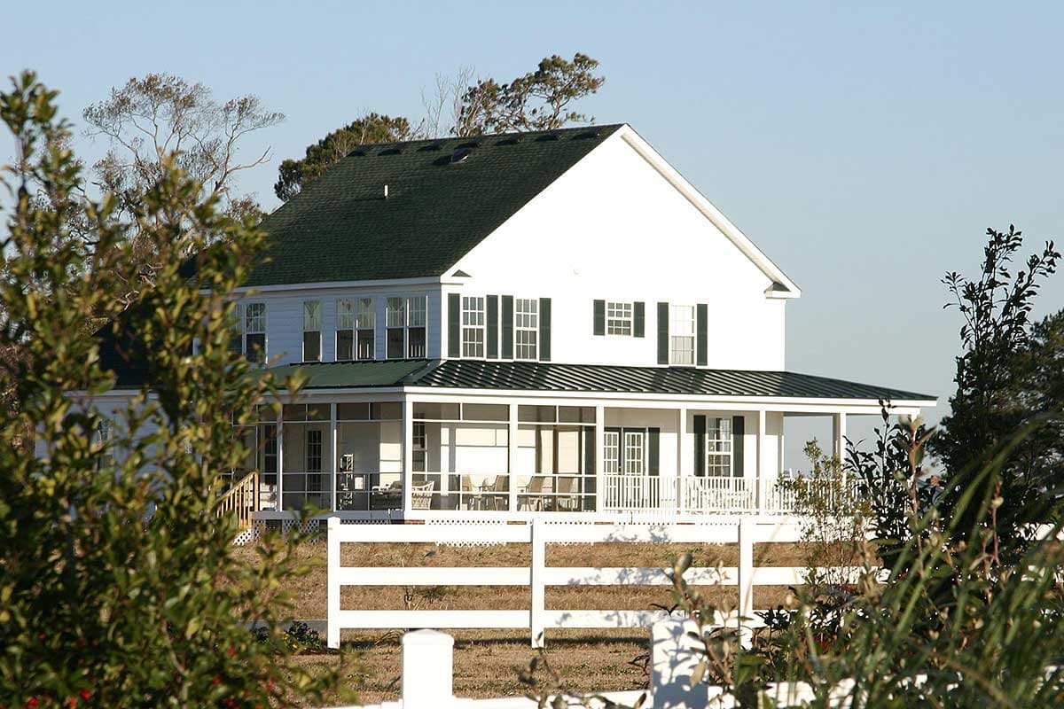 House plan exterior: Two-story home with a wrap-around screened porch, gable roof, and white picket fence.
