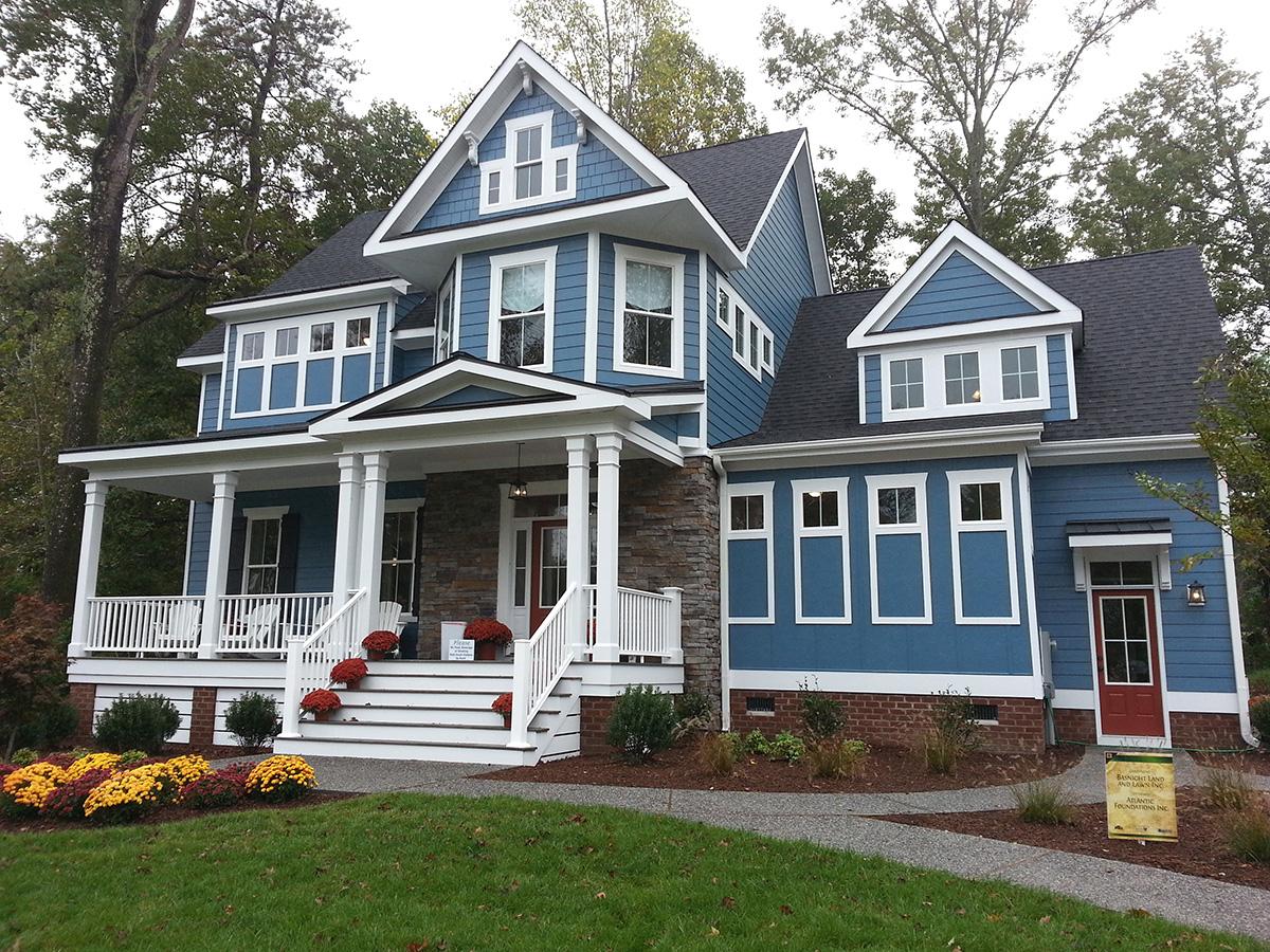 House plan exterior of a two-story blue home with a wrap-around porch, stone accents, multiple gables, and a red front door.