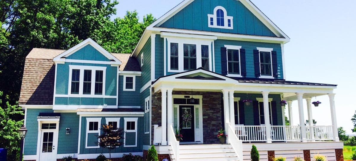 House plan exterior: Two-story home with varied gables, wraparound porch, stone accents, and arched dormer.