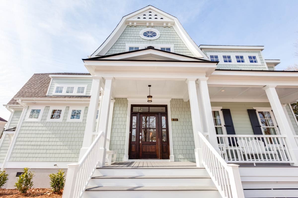 House plan exterior with covered porch, dormers, oval attic window, and shingle siding.