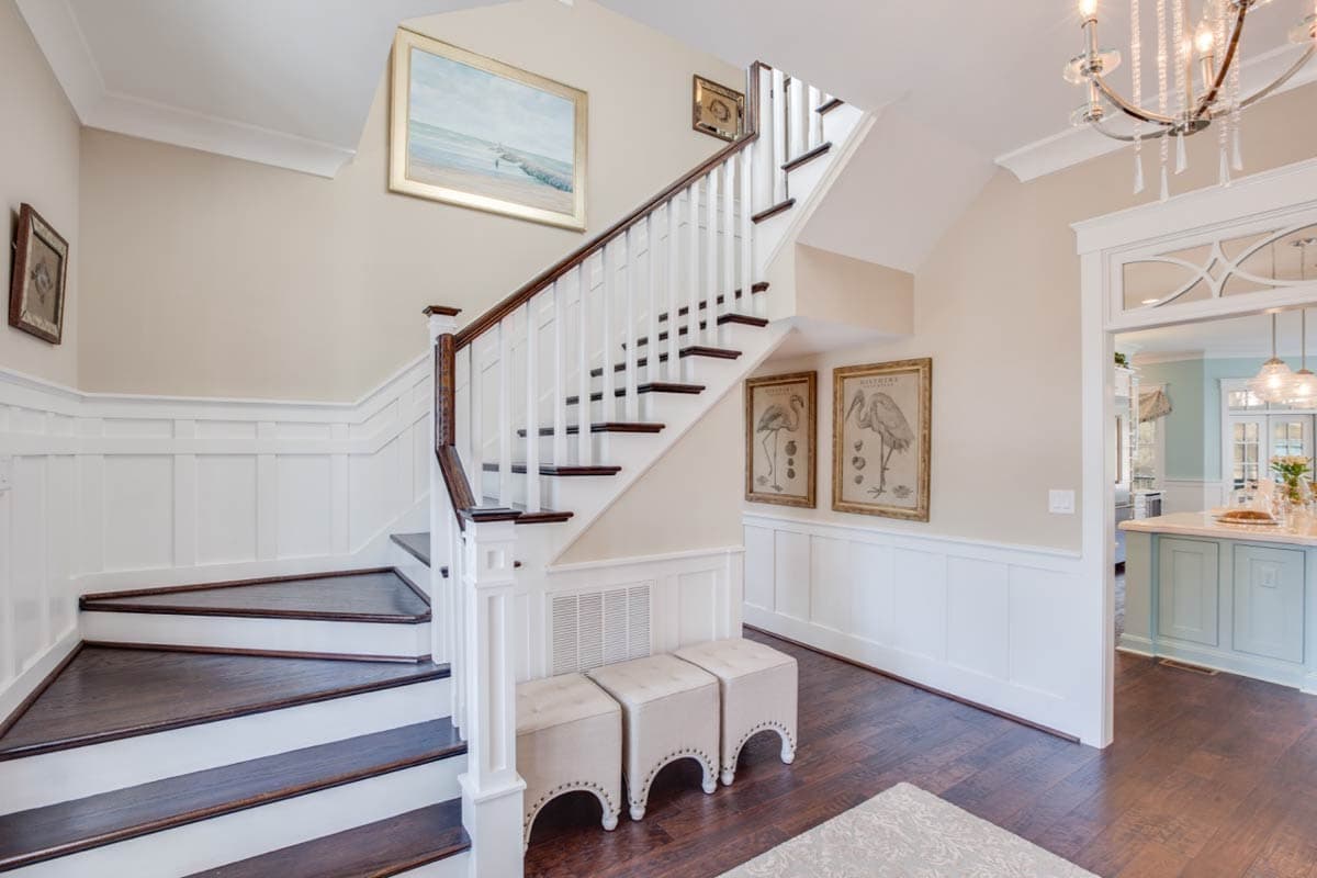 Interior view of a staircase with dark wood treads, white risers and balusters, wainscoting, and artwork.