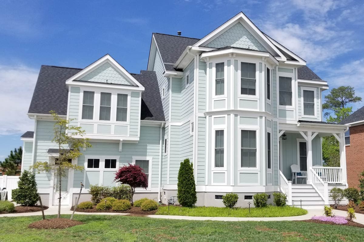 House plan exterior with light blue siding, white trim, multiple gables, bay windows, and a covered front porch.