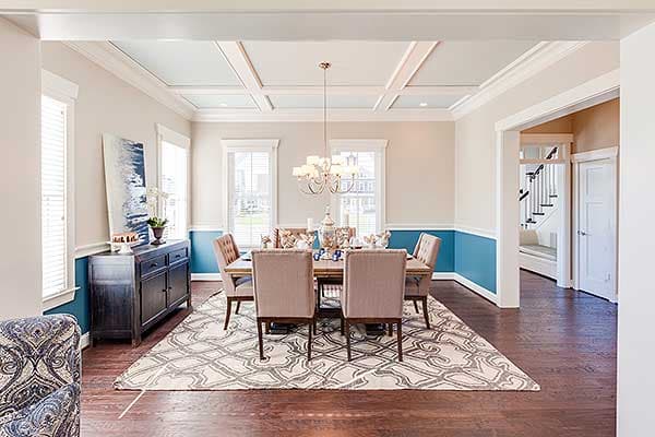 Dining room with coffered ceiling, chandelier, dining table, chairs, sideboard, and area rug.