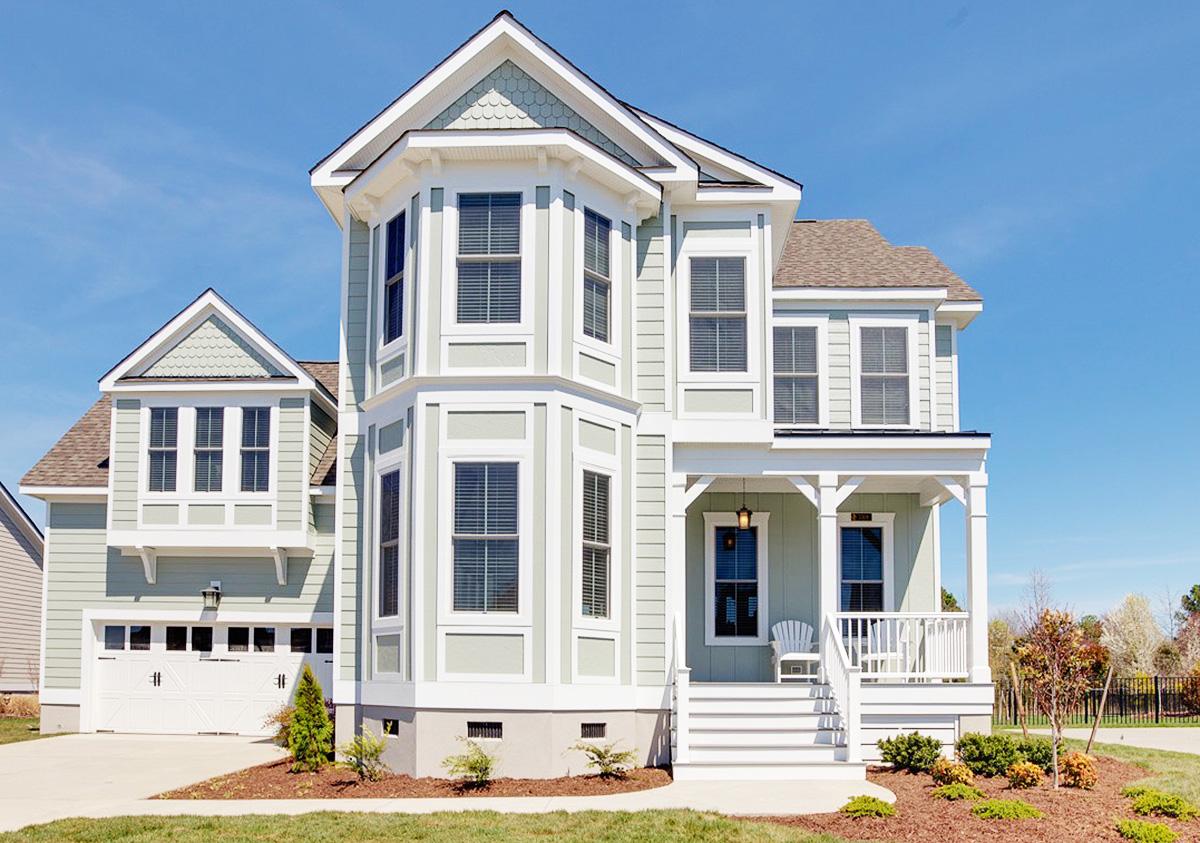 House plan exterior featuring a two-story home with bay windows, gabled dormers, and a covered front porch with white railings.