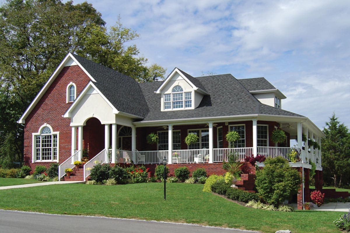 House plan exterior: two-story brick home with wraparound porch, gabled dormers, and arched window.