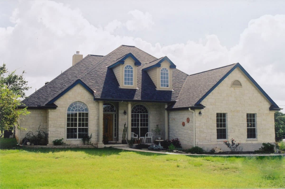 House plan exterior: Two-story stone house with arched windows, dormers, and a covered entrance.