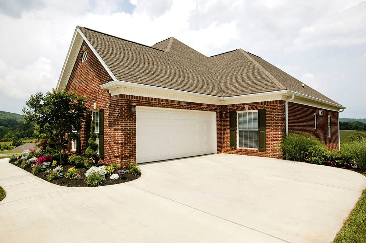Brick house plan exterior with gable roof, white garage door, and decorative landscaping.