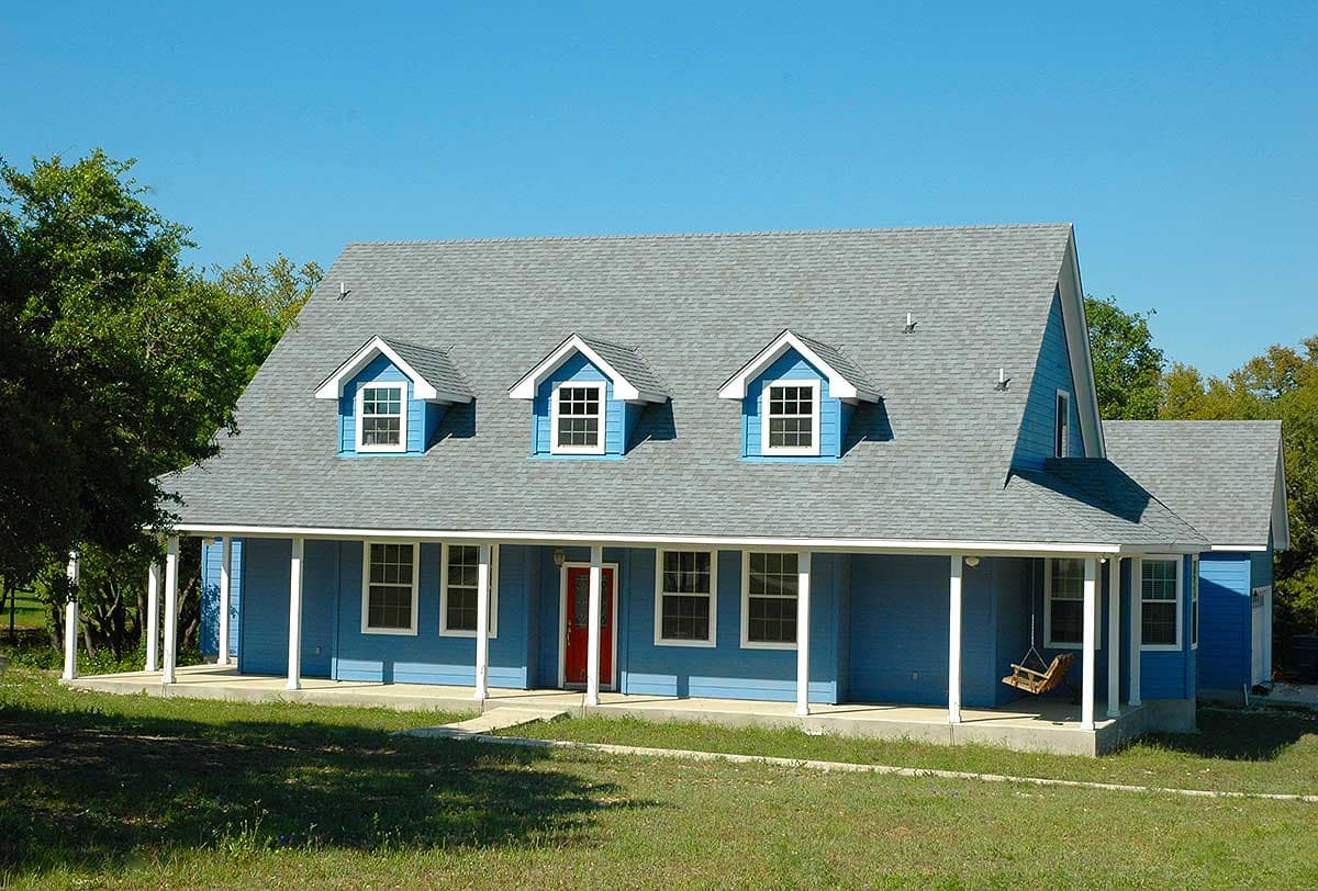 House plan exterior: Two-story blue home with a wraparound porch, three dormer windows, and a side-facing garage.