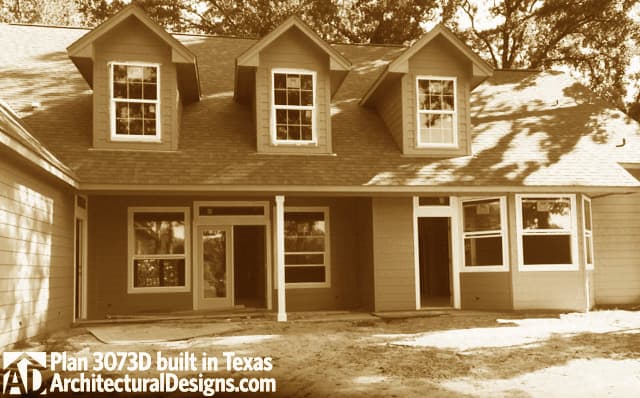 House plan exterior with three dormer windows, a covered porch with support columns, and bay windows.