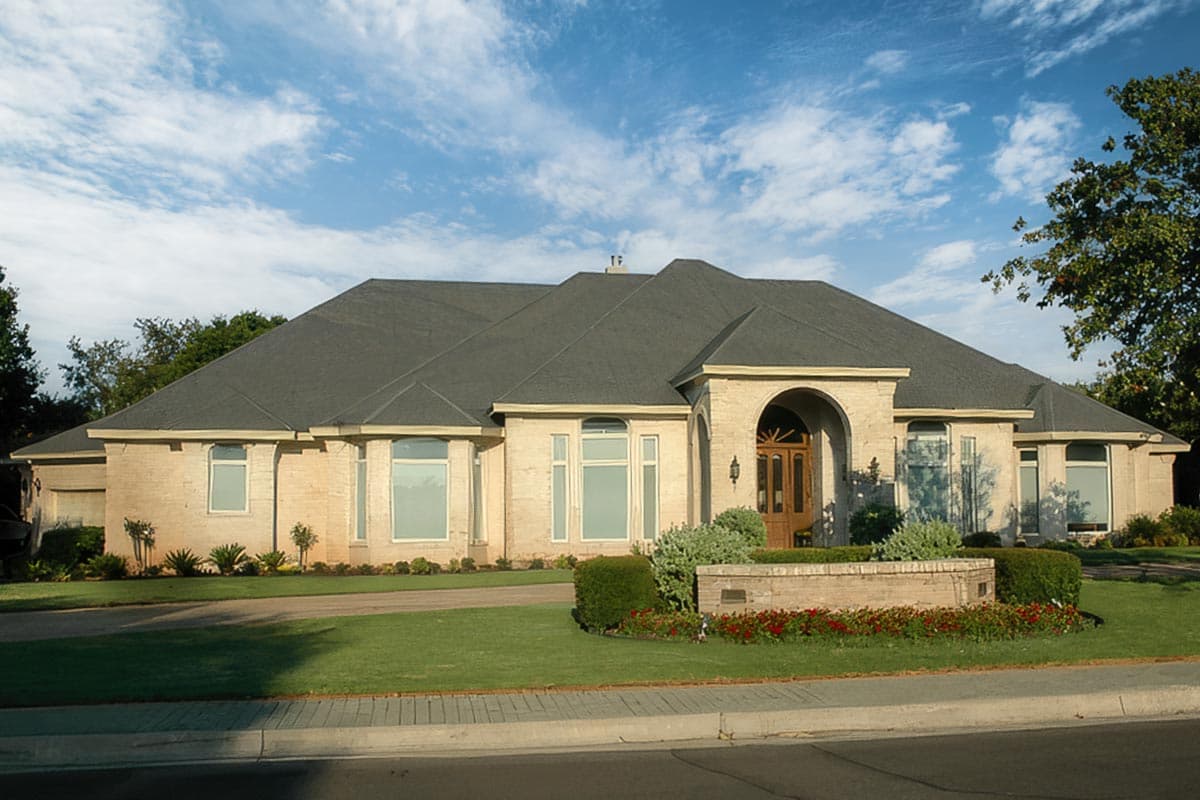 House plan exterior featuring a single-story ranch design with a dark shingle roof, arched entryway, and light brick facade.